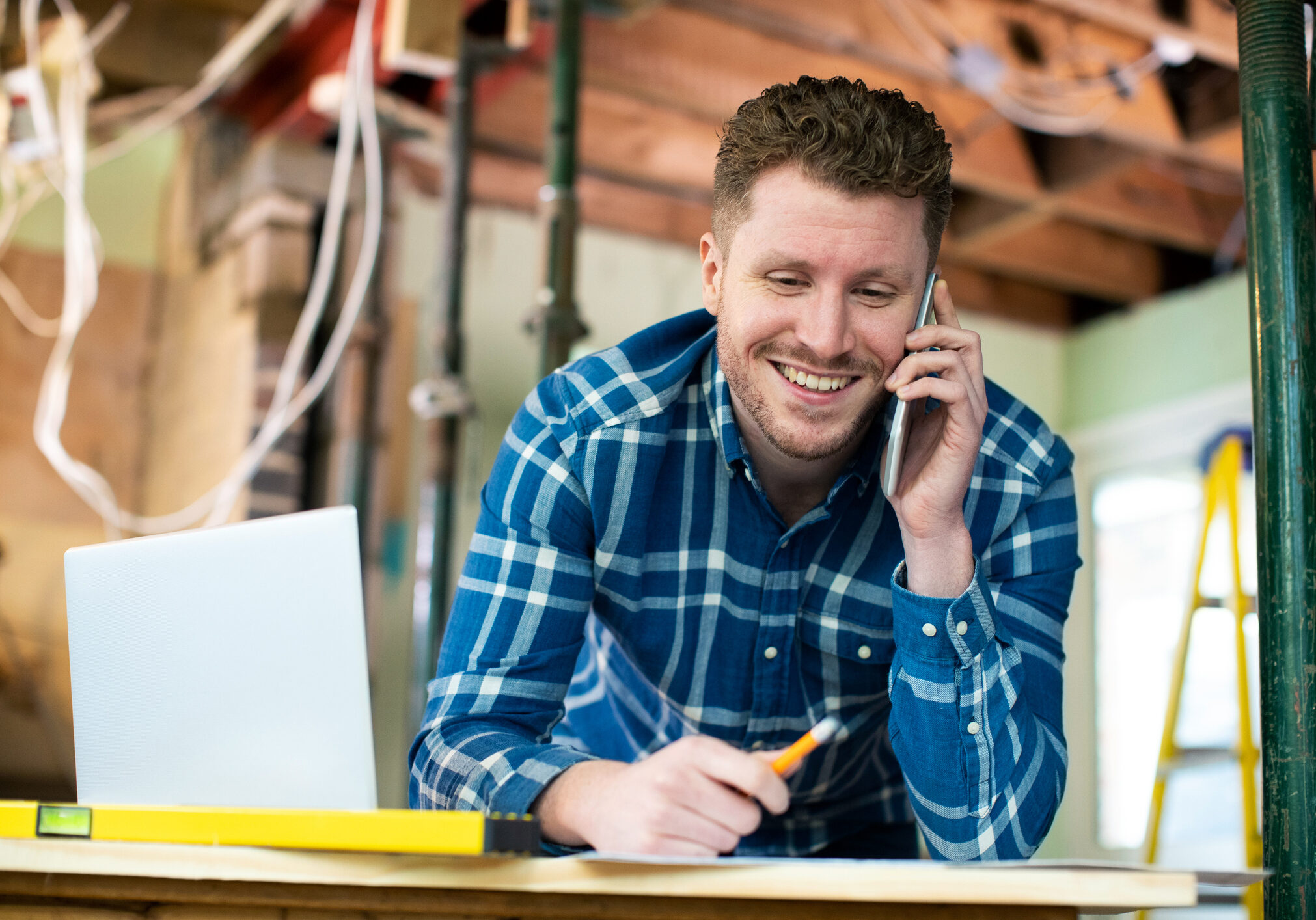 Architect Inside House Being Renovated Working On Plans Using Laptop And Talking On Cellphone
