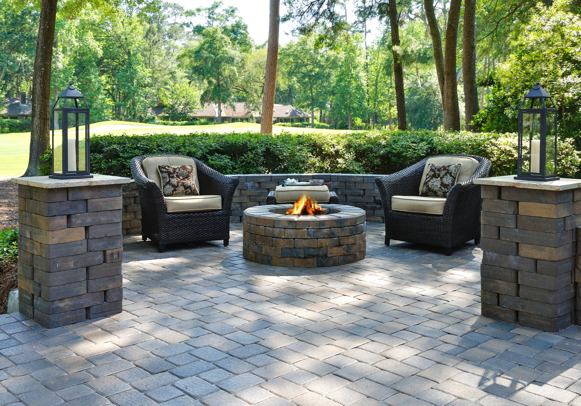 A beautiful outdoors pavers with two comfortable armchairs and a fire pit in a natural green environment
