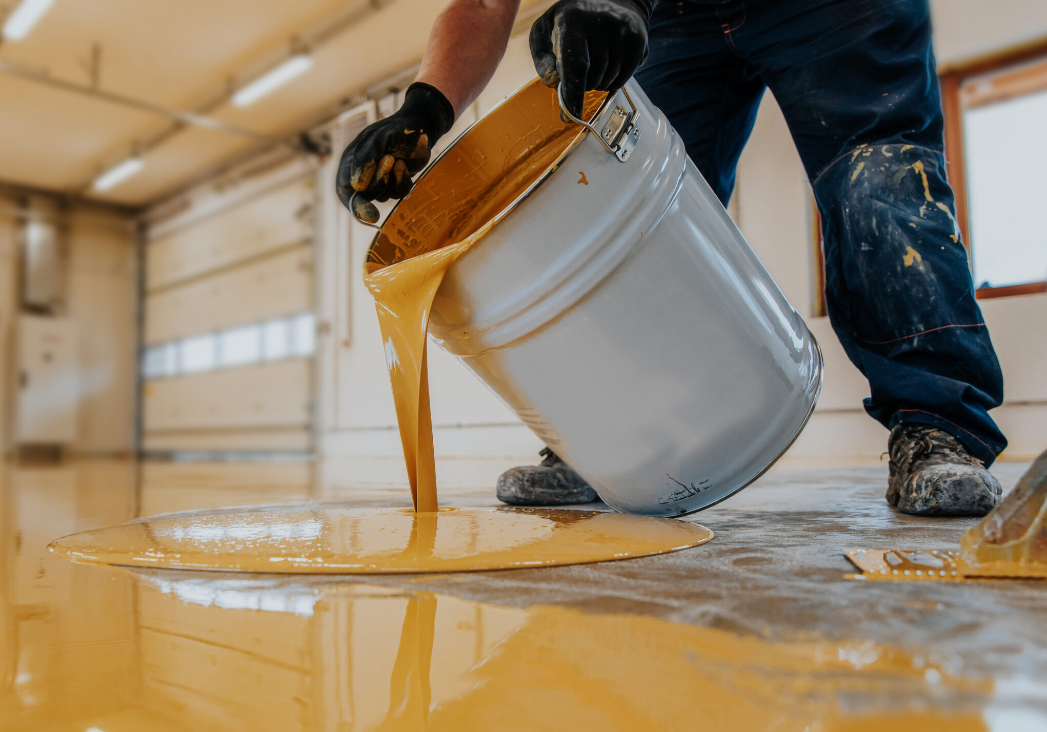 A closeup shot of a construction worker pouring out epoxy resin from a bucket onto a floor