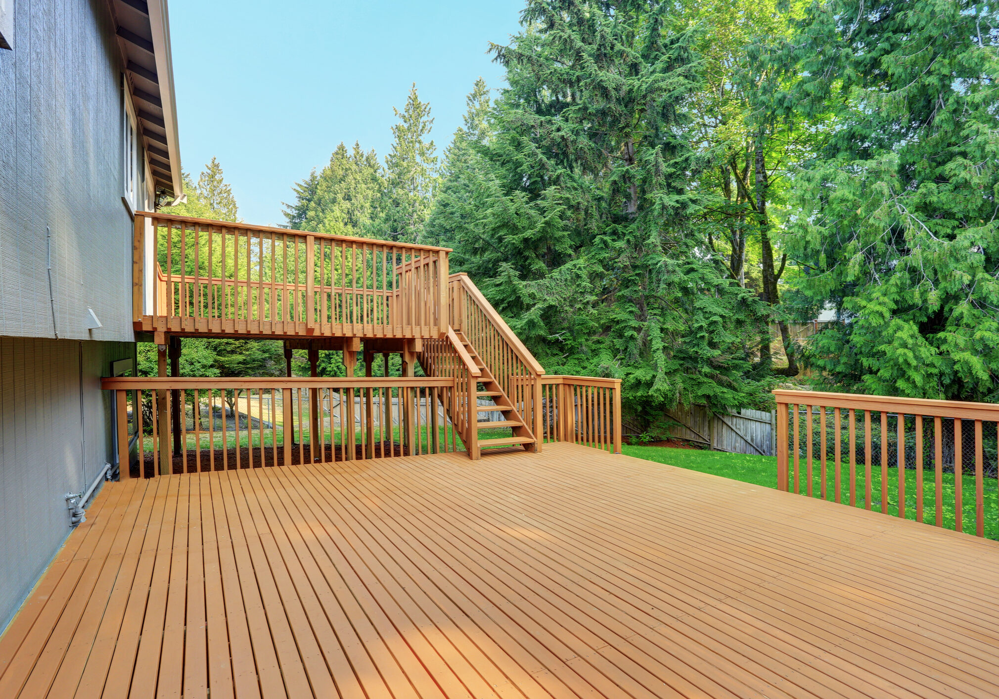 Backyard view of grey rambler house with upper and lower decks and green lawn. Kirkland, WA, USA.